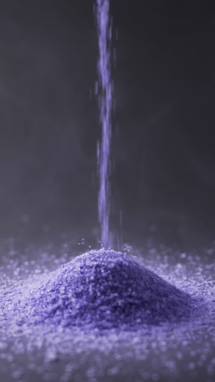 Vertical video of close up of heap of purple sand grains and copy space on black background