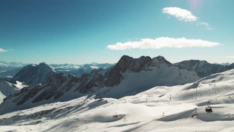 Drone-shot-of-ski-lifts-while-people-participating-in-winter-sports-in-the-background---Zugspitze,-Bavaria,-Germany