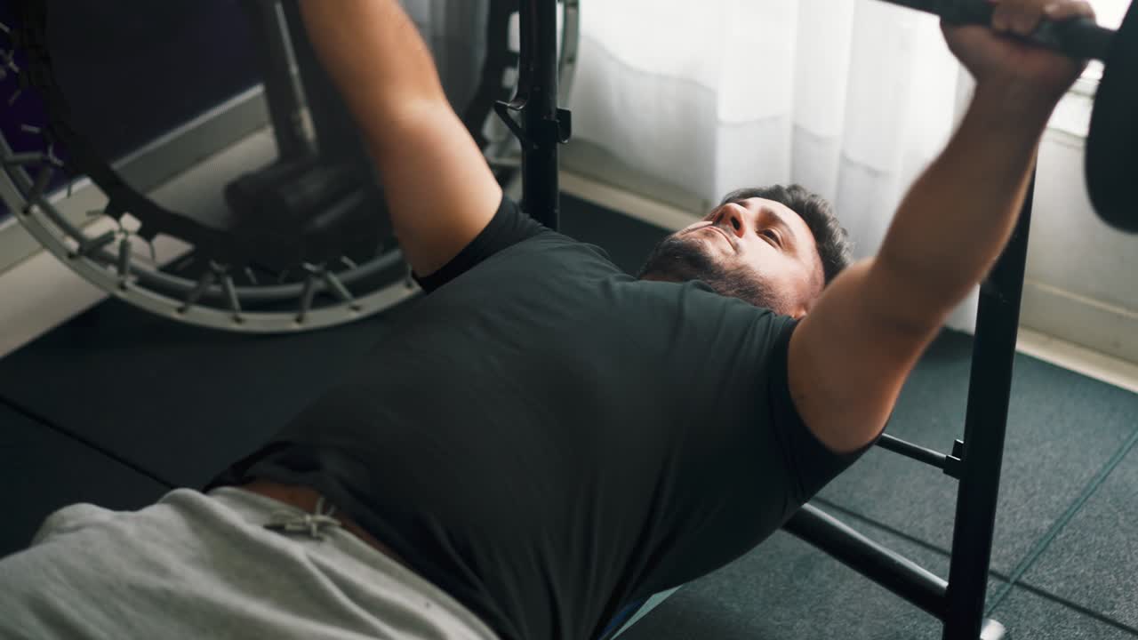 Fit genç bir adamın bench press'te ağırlık kaldırırken yana doğru kaydırma çekimi.