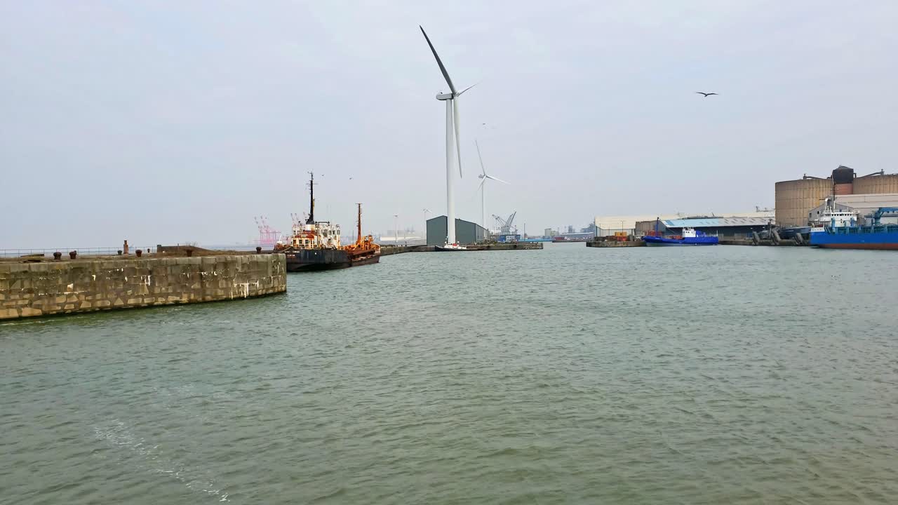 창고 옆 항구에 배가 정박해 있는 도크랜드의 풍력 발전소