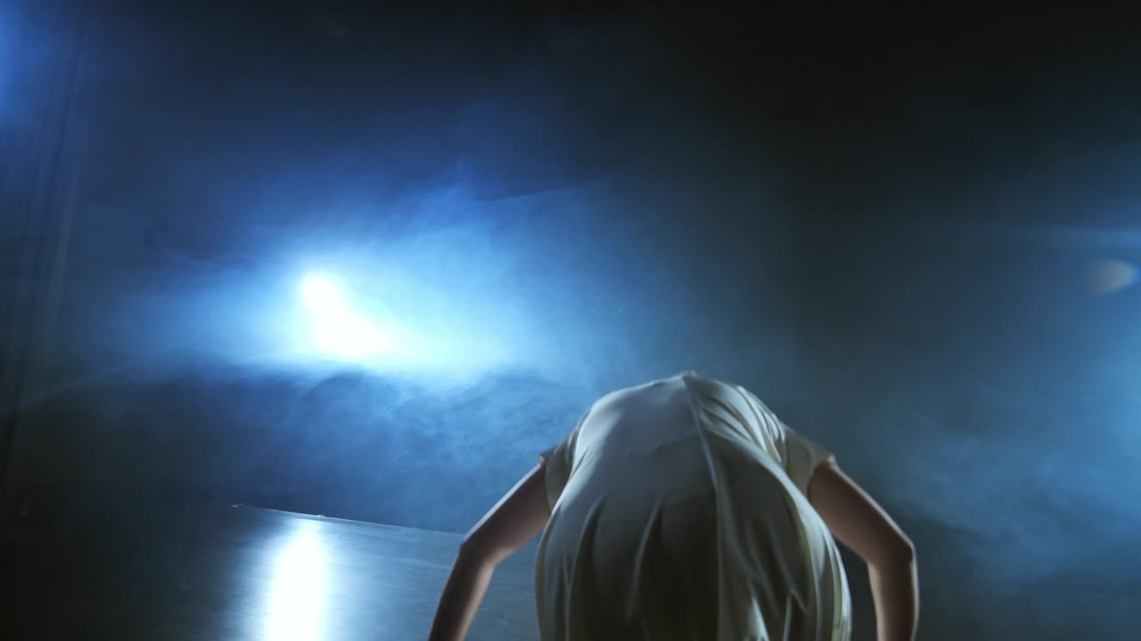 una mujer con un vestido blanco está bailando en el escenario los bailes dramáticos del ballet moderno. una bailarina de ballet mueve plástico realizando coreografía moderna en humo