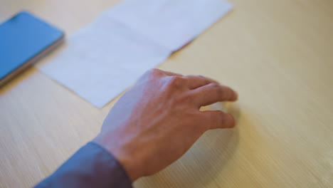 close-up of young man's hand gently resting on wooden table near white napkin, fingers softly curved in natural position, expressing quiet stillness, mindfulness, and emotional calm in warm indoor setting