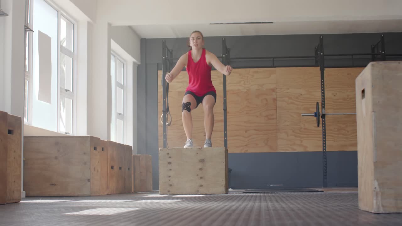 Donna caucasica concentrata che esegue salti sul box, cross training in palestra, al rallentatore.