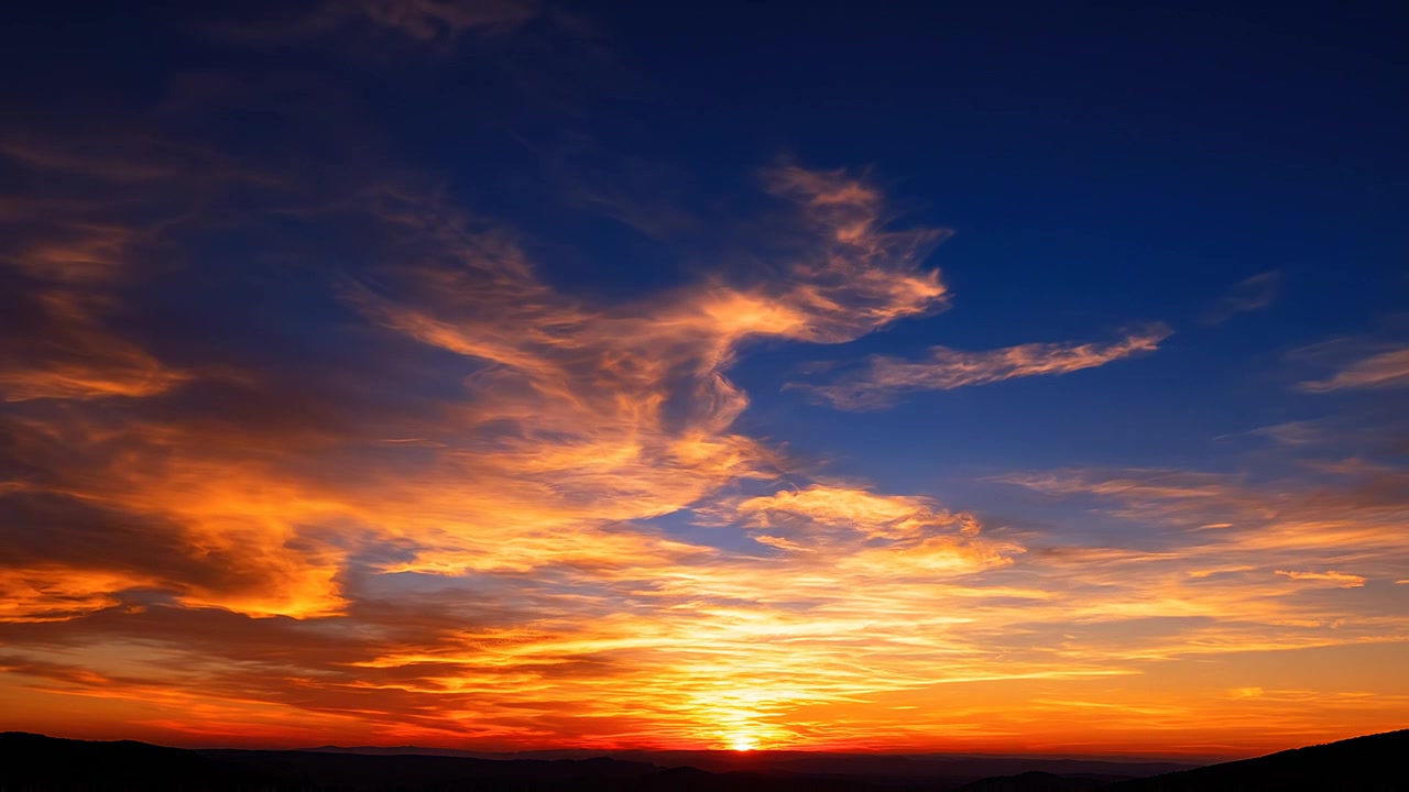 Levende orange solnedgang over mørke bjergsilhuetter under blå himmel