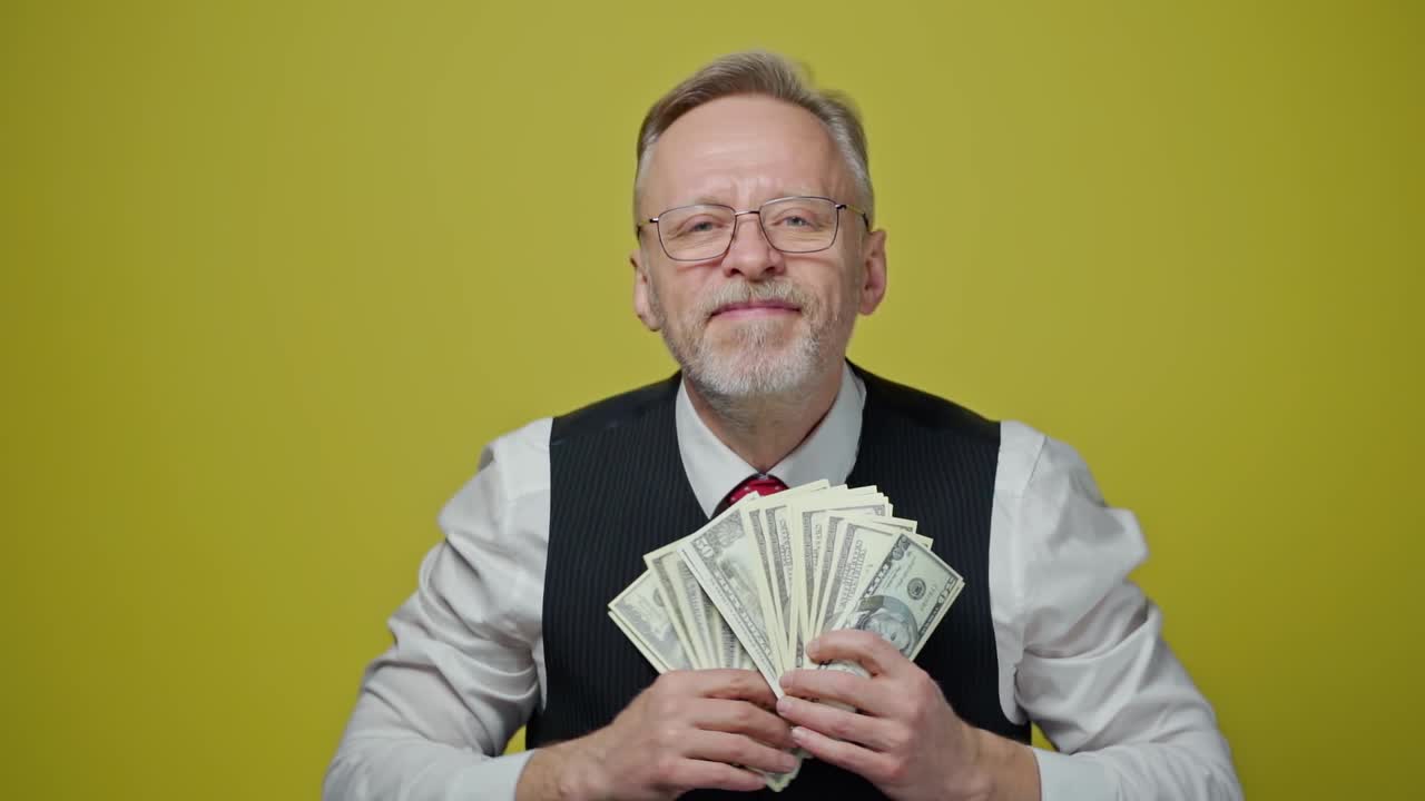 Happy senior businesman waving dollar banknotes.Rich grey-haired man holding big amount of money in his hands and showing them on the camera.