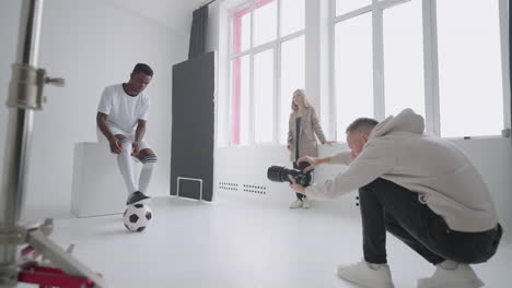 behind-the-scenes photo shoot: a photographer in a photo studio uses a flash for photos of a black professional football player. photo shoot in the studio of a sports magazine advertising