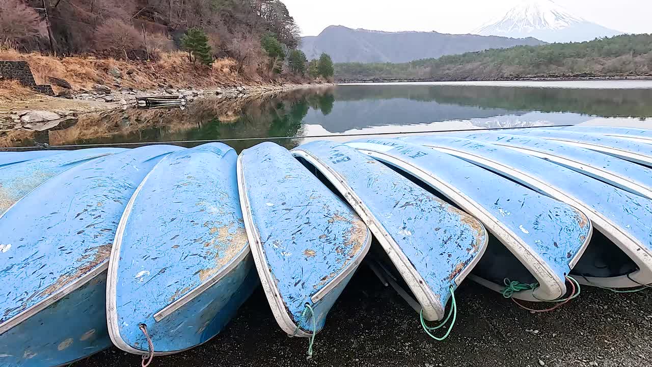 A row of blue boats lies on the shore of Lake Kawaguchiko, Japan, under soft daylight with a serene mountain backdrop