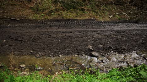 Der-Bach-Fließt-Unterhalb-Einer-Schlammigen,-Unbefestigten-Straße,-Die-Von-Schweren-Maschinen-In-Die-Landschaft-Gehauen-Wurde