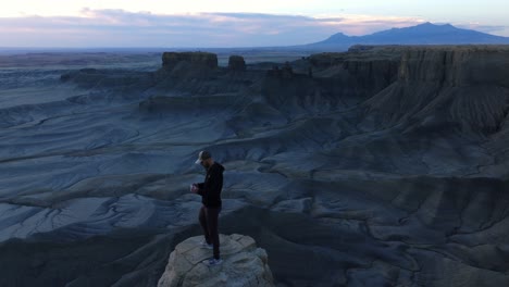 hombre de pie en una roca pilotando un dron sobre el increíble paisaje lunar de factory butte en utah, estados unidos