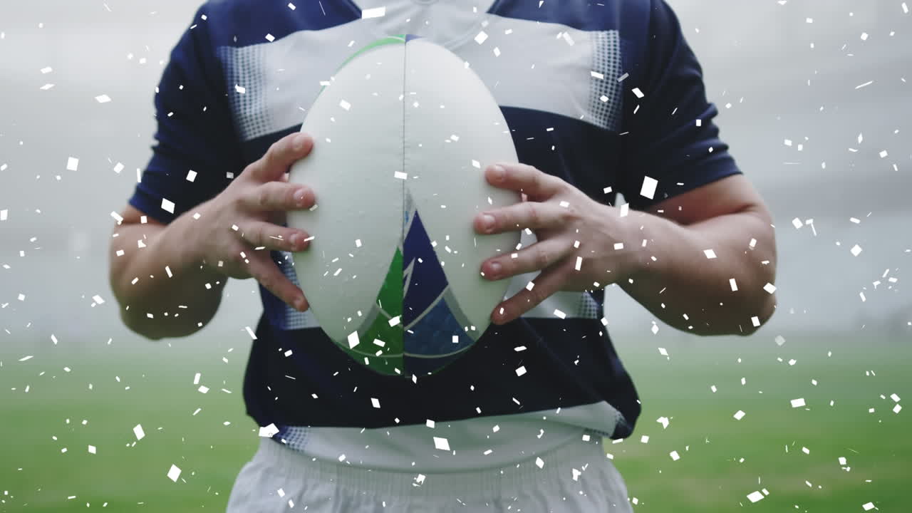 Animation of white confetti falling over biracial male rugby player holding a rugby ball