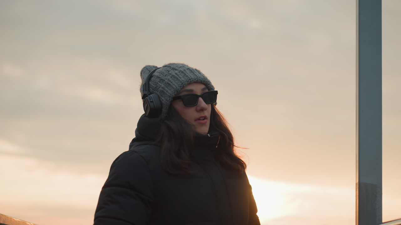 Urban sunset listening. Silhouette of calm rooftop music. Listener in headphones gazes at horizon. Person wearing headphones enjoys peaceful music while observing city skyline at dusk