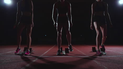 three girls in black clothes are in the starting pads to start the race in the competition in the light of the lights and run towards the finish