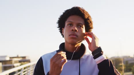 african american man putting earphones on during exercise outdoors