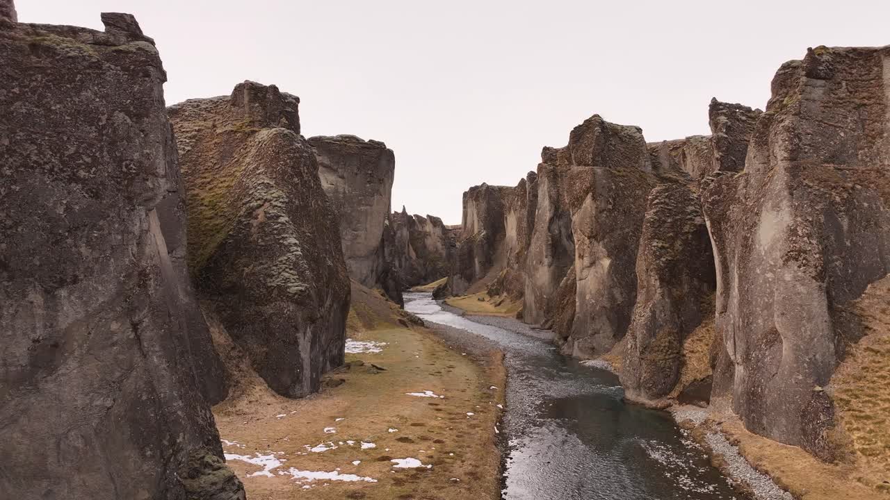 Aerial shot moving through the dramatic Fjaðrárgljúfur Canyon, Iceland. River winds between towering cliffs. Majestic Nordic scenery.
