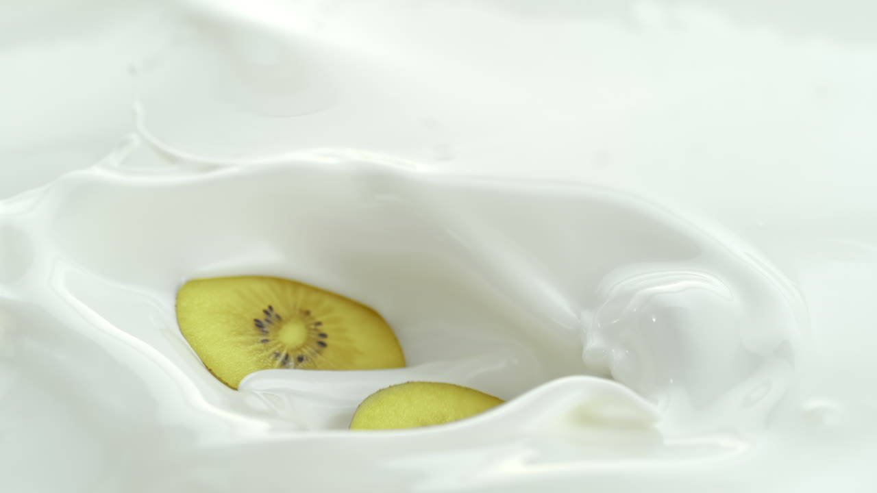 키위 조각이 크리미한 우유에 떨어지고 매크로와 느린 동작으로 스프레이를 만니다.
