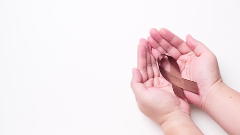 Male-hand-holding-ribbon-in-brown-color-on-white-background