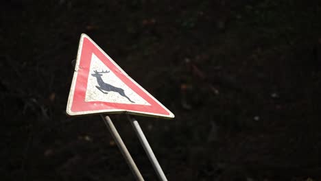 Deer-crossing-sign-in-red-and-white-triangle-is-cracked-and-hit-at-an-angle,-car-drives-by-in-front