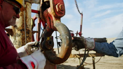 workers hold the huge heavy metal hook from the crane. men set the equipment for oil and gas production.