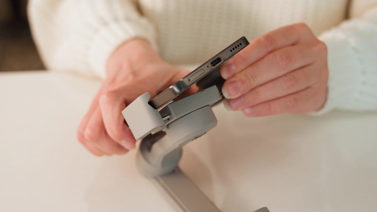 Close-up hands align and press adhesive tab onto padded wrist strap resting on support, revealing bending hinge movement, textured knit sleeve, and soft indoor tabletop lighting, with hand, wrist