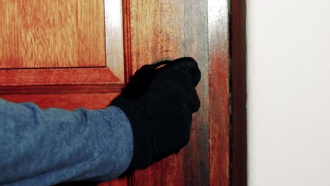 hombre con un guante negro lentamente cierra una perilla de latón en una puerta de madera
