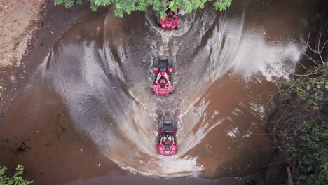 overhead shot of six atvs creating water splashes while crossing a muddy puddle in the forest in costa rica.