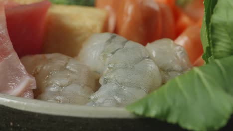 close up of a pot of shabu ingredients spinning around on the black background