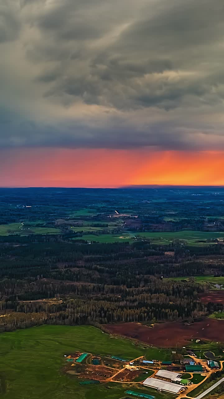 Sunset glows beneath dark storm clouds with rain over farmland in drone hyperlapse, vertical