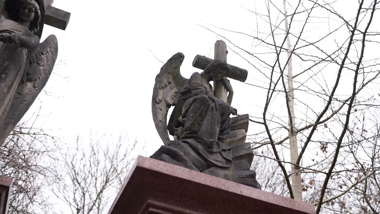 cruz y estatua en una lápida cubierta de musgo y hojas verdes en un cementerio forestal en un día nublado