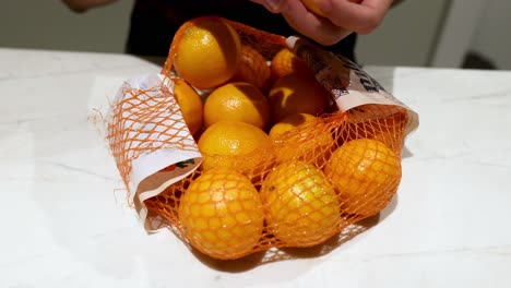 hands arranging oranges in a net bag