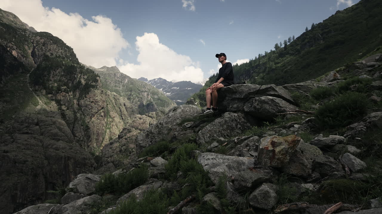 Man Sitting on Rocks in Mountain Valley