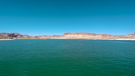 A-houseboat-in-the-distance-is-docked-on-the-sandy-shore-of-Lake-Powell,-Page,-Arizona