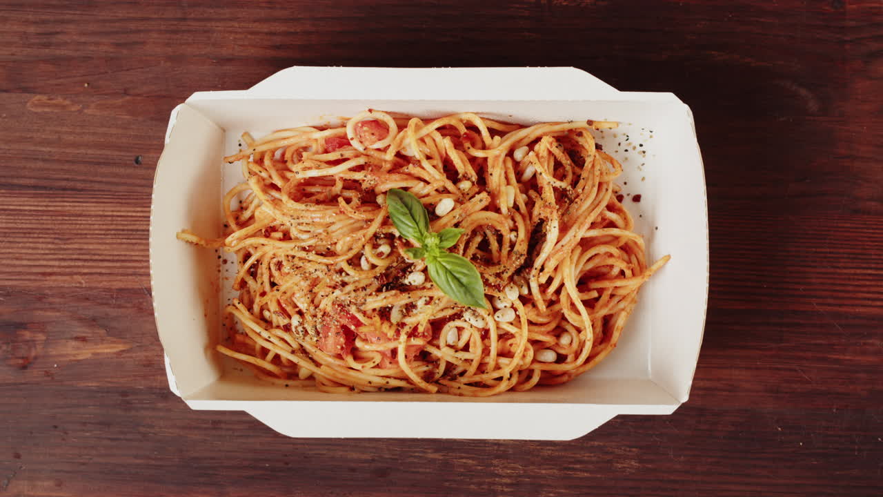 Mano che condisce e guarnisce spaghetti al basilico in un contenitore da asporto