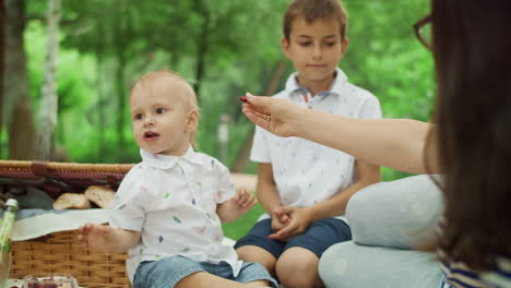 mother feeding small son with cherry in park. family having picnic outdoors