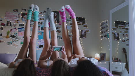 Chicas-Adolescentes-Felices-Acostadas-En-La-Cama-En-Casa-Con-Las-Piernas-Arriba-Divirtiéndose-En-Pijamas-Tomando-Fotos-Usando-Un-Teléfono-Inteligente-Disfrutando-De-Una-Relajante-Mañana-El-Fin-De-Semana