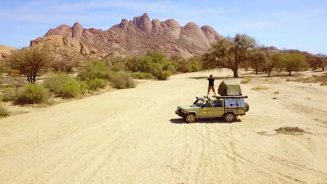 aerial over a man standing on a 4wd safari camper van taking photos of rock formations at spitzkoppe namibia africa