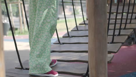 child walking on a wooden playground bridge