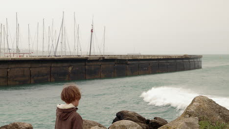 niño arrojando una roca al océano ondulado