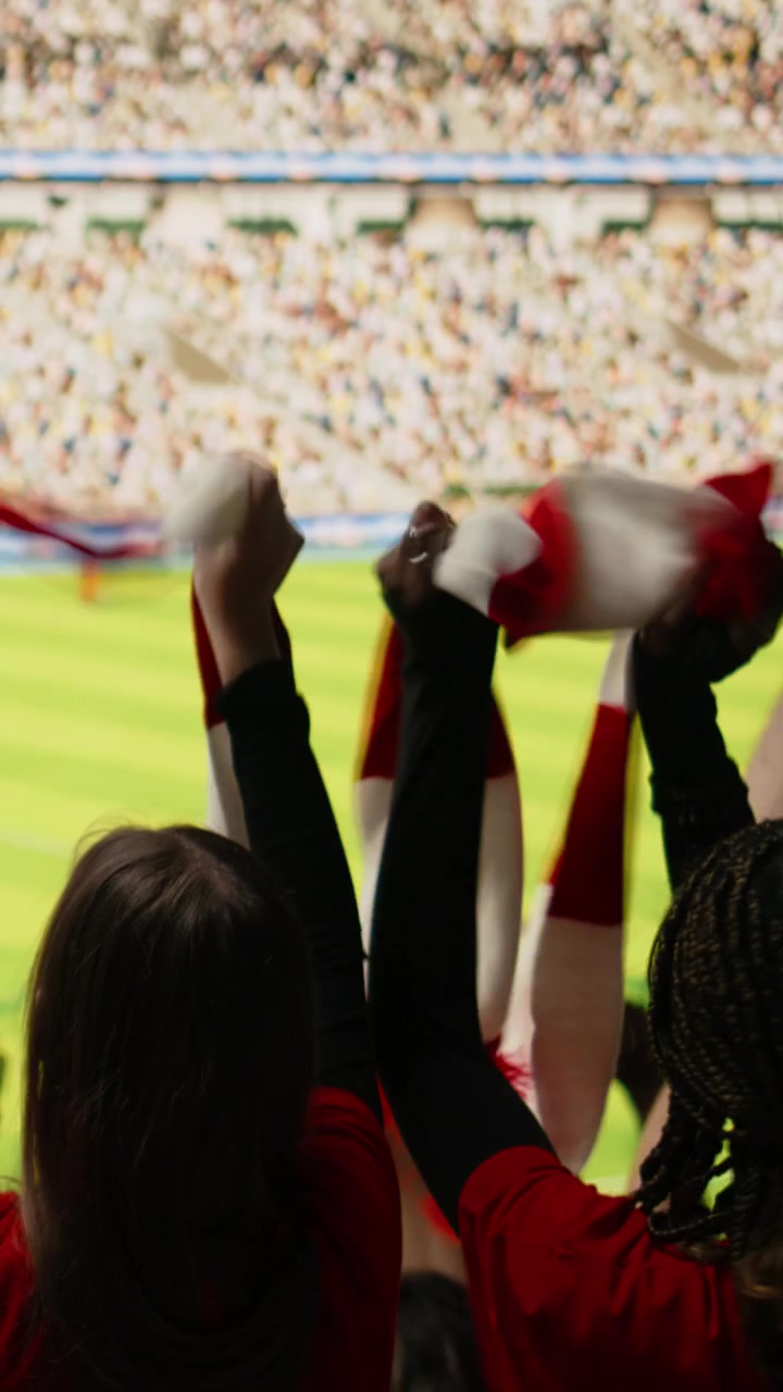 Video vertical: Vista trasera de un ruidoso grupo de aficionados celebrando un gol dramático durante un partido en vivo.