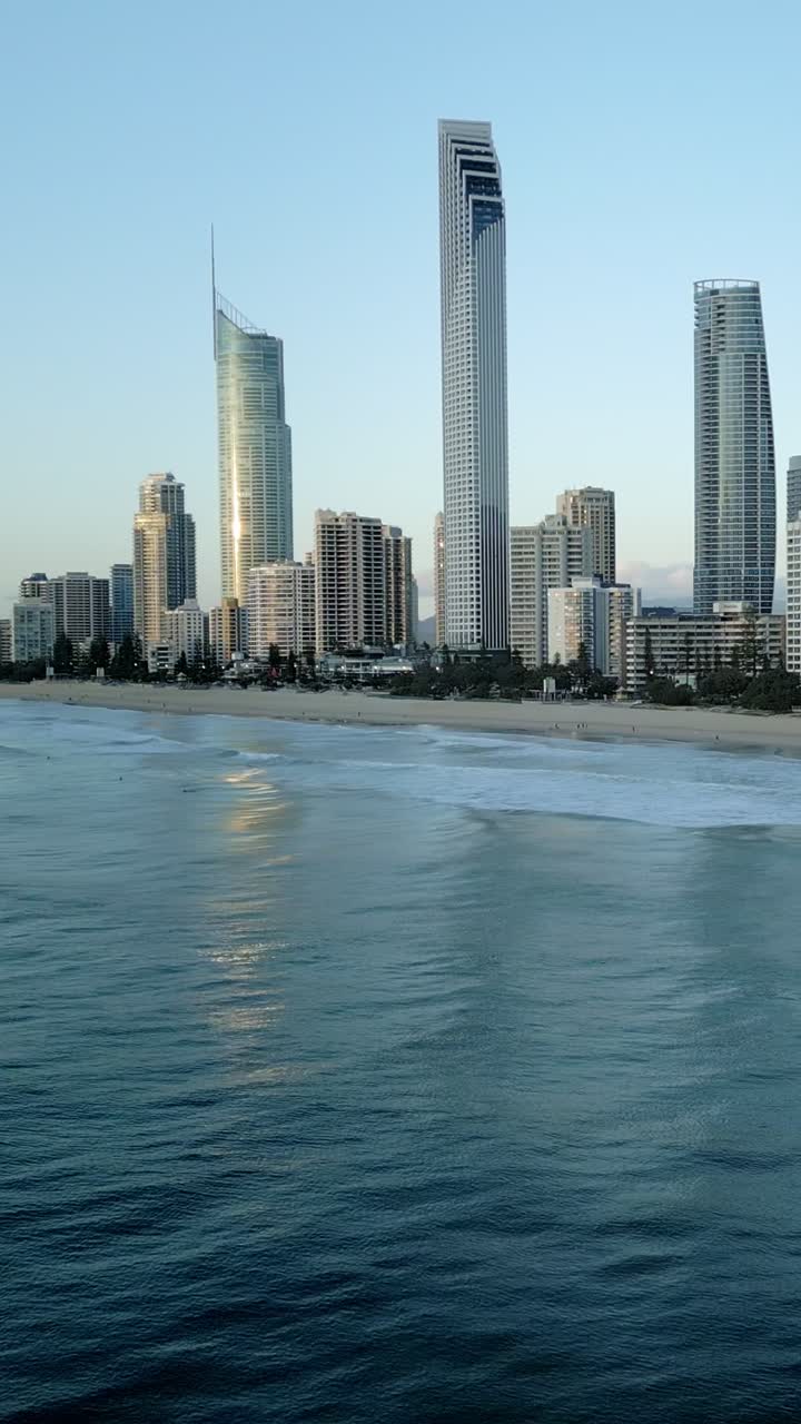 Vertical drone of ocean waves rolling with surfer wave riding, skyline background, Surfers Paradise Gold Coast Queensland Australia. Active surf lifestyle showcasing beach culture and coastal paradise