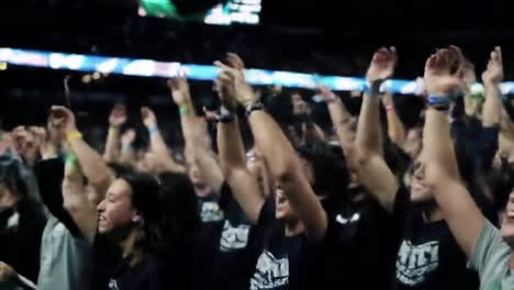 crowd of enthusiastic fans in dark stadium celebrating with arms raised, capturing the excitement and energy of a thrilling live event experience