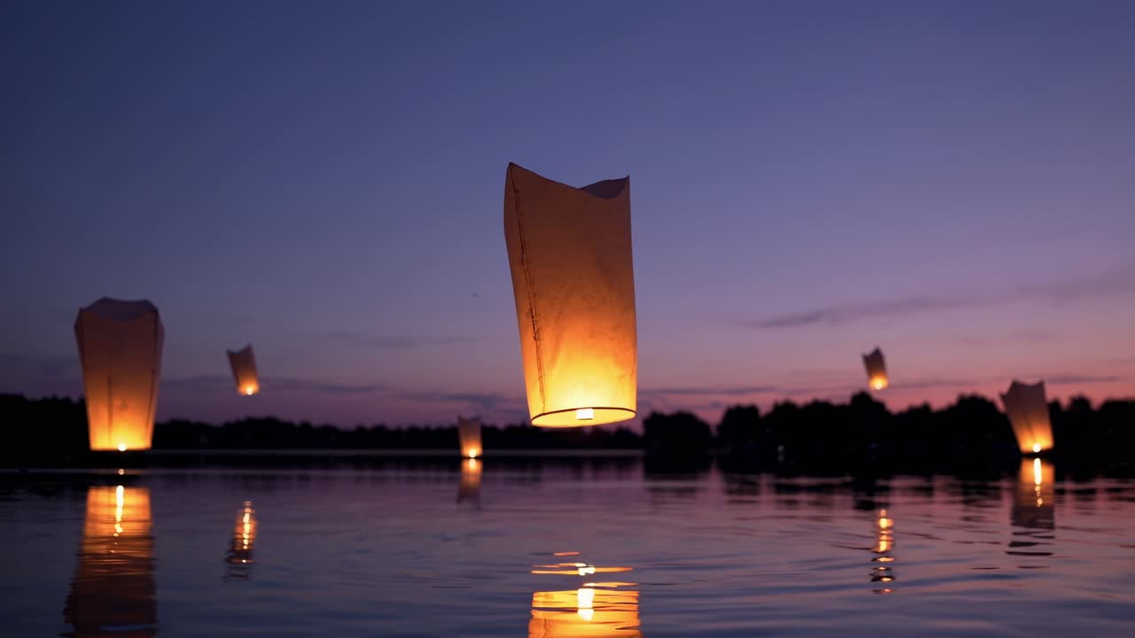 Sky lanterns floating peacefully, casting warm glows across tranquil lake surface during twilight, reflecting soft illumination on water's mirror like expanse