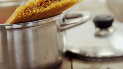 raw spaghetti arranged in silver pot on wooden table with the lid