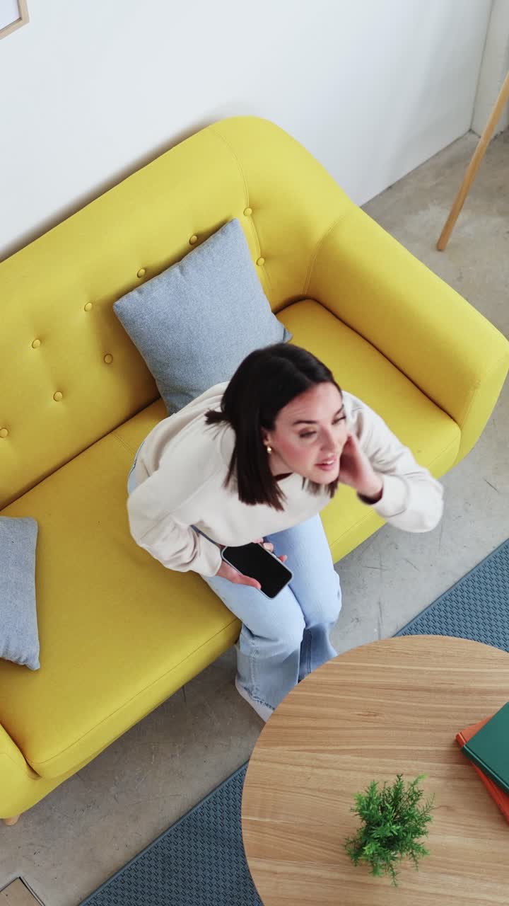 Ung kvinde sidder på gul sofa og bruger smartphone