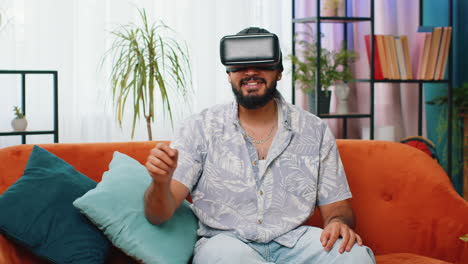 Indian-man-using-virtual-reality-futuristic-technology-headset-play-simulation-3D-video-game-at-home