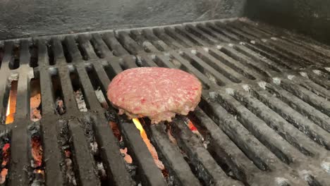 raw hamburger patty cooking on a flame lit grill