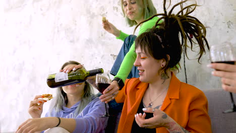 happy woman with tattoos and dreadlocks pouring wine for a friend during a party at home