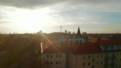 Low-flight-above-Berlin,-Germany-residential-neighbourhood-street-and-rooftops-towards-City-center-with-TV-Tower-Skyline,-Scenic-Autumn-vibe-Aerial-Dolly-in