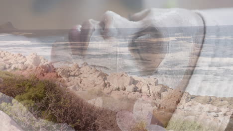 animation of rocky coast and sea over relaxed african american woman wearing beauty face mask