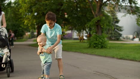 elder brother helping junior to walk outdoors. family walking in summer park