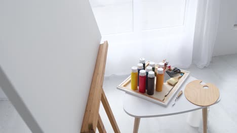jars with colored paints bones and spatulas stand on the artist's desk near the easel - jars with colored paints bones and spatulas stand on the artist’s desk near the easel with white canvas. plastic containers with different paints belonging to the artist. the workshop is very bright